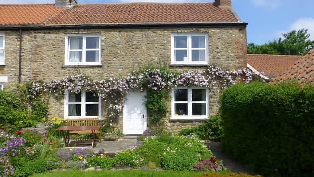 Charming stone cottage with white windows, surrounded by lush greenery and colorful flowers in Catterick, North Yorkshire.