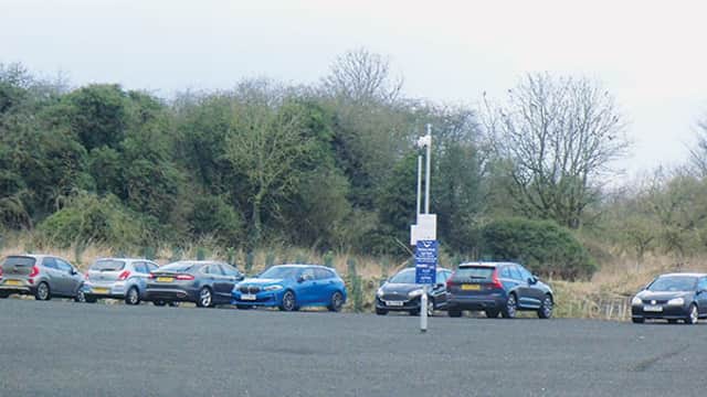 Cars parked in a gravel lot with trees in the background, featuring a sign for Station Road Car Park.
