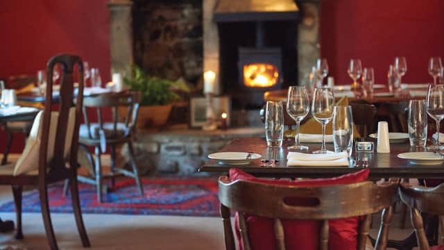 Cozy dining area with wooden tables, elegant glassware, and a warm fireplace against a rich red wall.