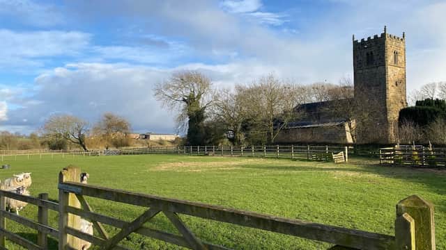 A scenic view of a church tower beside a green field and wooden fence under a blue sky in Danby Wiske, Yorkshire.