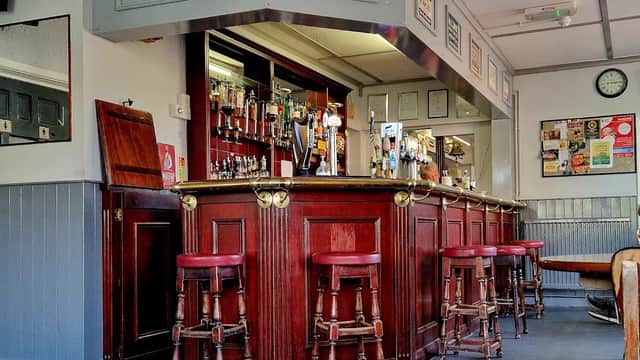Wooden bar with red stools, mirrors, and various drink taps; walls adorned with notices and a clock.