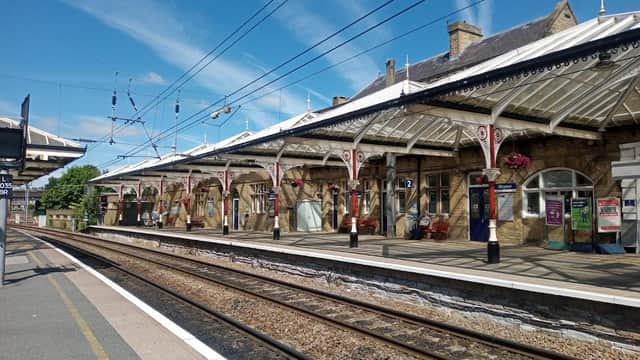 Bus station in Skipton, Yorkshire, featuring a stone building, platforms, and decorative canopies under a blue sky.