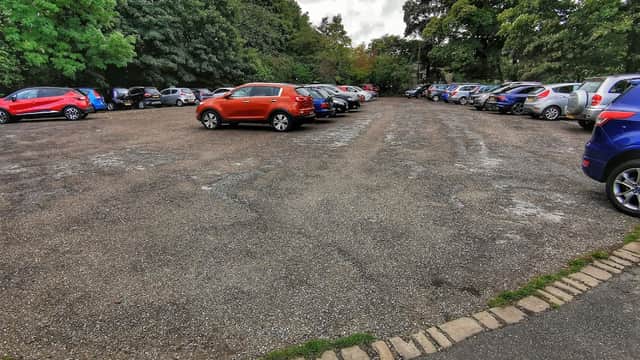 Free parking lot at Warrens Ln, Birstall, with various parked cars and trees lining the background.