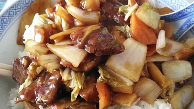 A bowl of stir-fried vegetables and meat in sauce served over rice, with chopsticks on the side.