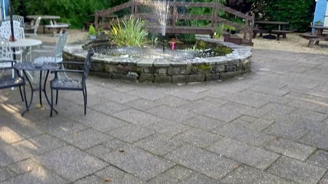 A courtyard with a stone fountain surrounded by greenery, picnic tables, and patio seating under umbrellas.