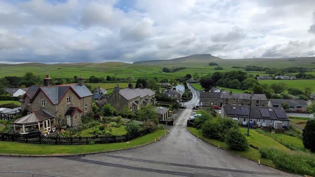 Scenic view of Horton-in-Ribblesdale with quaint houses, lush greenery, and rolling hills under a cloudy sky.