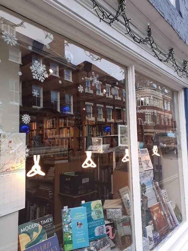 Bookshop window displaying books, snowflake decorations, and warm lighting, with reflections of nearby buildings.