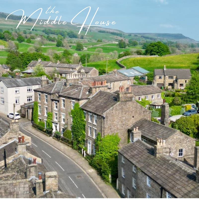 Aerial view of Middle House in Askrigg, surrounded by stone buildings and lush green hills in Cubeck, Yorkshire.