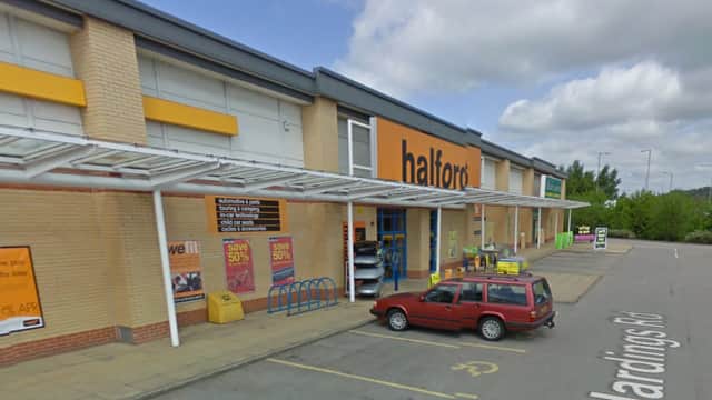 Halfords store exterior in Keighley, featuring bike racks, promotional signage, and a parked red vehicle.