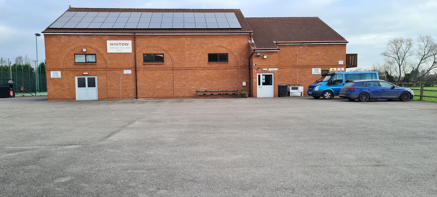 Wistow New Jubilee Village Hall with solar panels, parking area, and a blue vehicle beside the entrance.