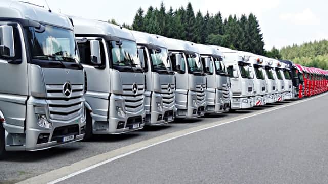 Row of silver trucks parked neatly along a road, surrounded by trees in the background.