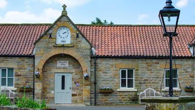 Stone building with a clock, date 1992, and flower baskets, alongside a traditional lamppost and benches.