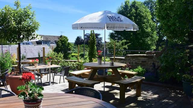Sunny outdoor seating area at The Galphay Inn, featuring picnic tables, potted plants, and a large umbrella.