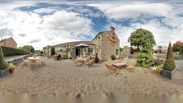 Black Horse Inn in Fencote, Yorkshire, features outdoor seating, potted plants, and a charming stone building under a cloudy sky.