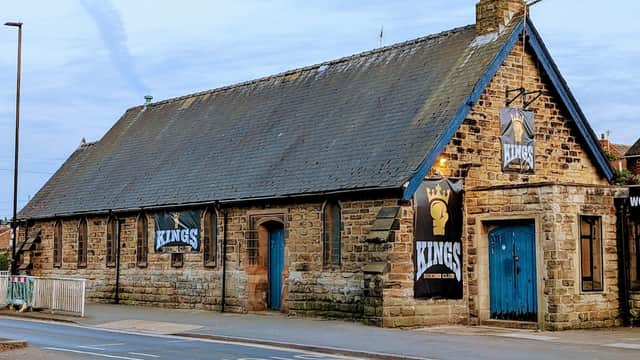 Historic stone building with blue doors and banners for "Kings" on the exterior, set along a street in Woodhouse.