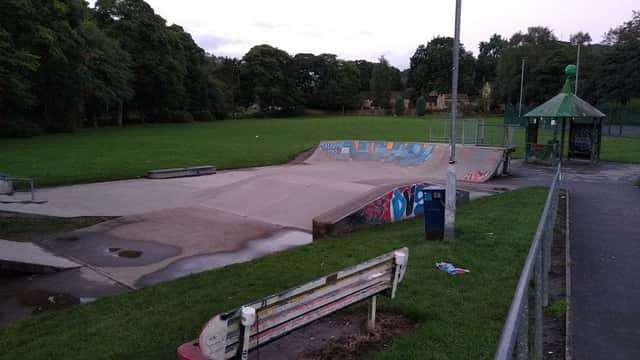 Skate park with a concrete ramp, colorful graffiti, green grass, and a nearby bench under a cloudy sky.