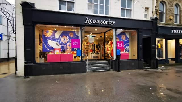 Storefront of Accessorize with colorful displays and signage, featuring promotions and a wet pavement outside.
