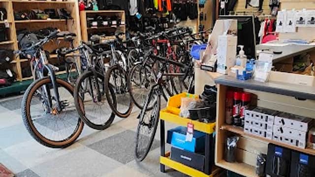Bikes on display in a shop with shelves of cycling gear and accessories in a spacious, well-lit interior.