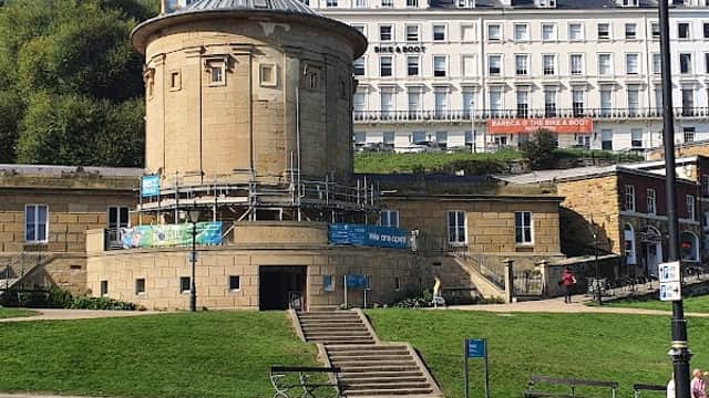 Historic building with a round tower, scaffolding, and green lawns, set against a blue sky in Osgodby, Scarborough.