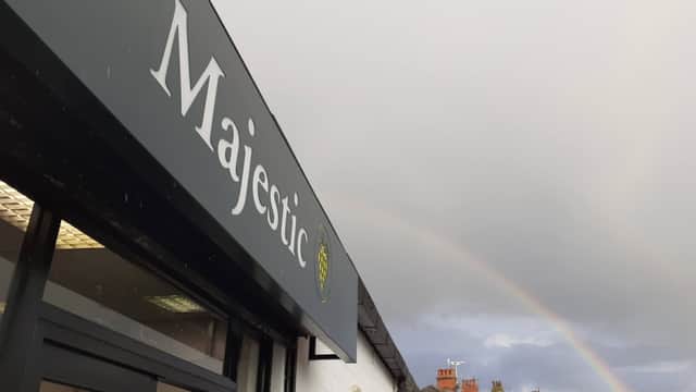 Sign for Majestic Wine with a rainbow in the cloudy sky above, showcasing a typical Harrogate street scene.