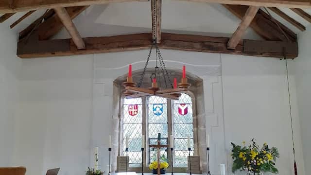 Interior of Bewerley Grange Chapel featuring wooden beams, stained glass windows, altar, and floral arrangements.