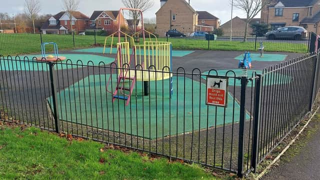 Colorful playground equipment within a fenced area, featuring a spinning structure and slides on green flooring.