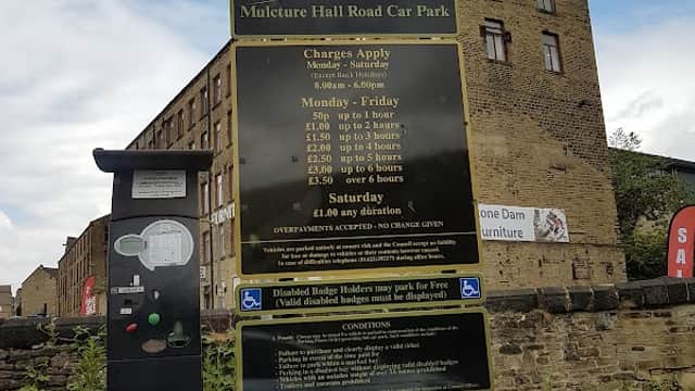 Welcome sign for Mulcture Hall Road Car Park, with payment machine and parking fees displayed, set against a brick building.