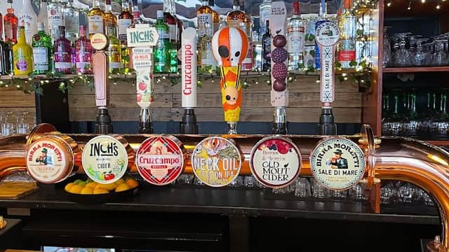 Colorful beer taps lined up on a wooden bar, with various brands and drinks visible, surrounded by bottles and festive decor.