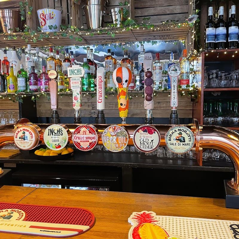 Colorful beer taps lined up on a wooden bar, with various brands and drinks visible, surrounded by bottles and festive decor.