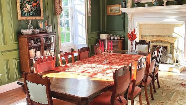 Elegant dining room with a long wooden table, antique chairs, green walls, floral artwork, and a chandelier.
