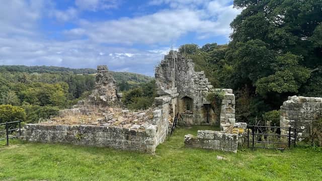 Ruined stone structure surrounded by lush greenery and trees under a partly cloudy sky in Mulgrave Woods.