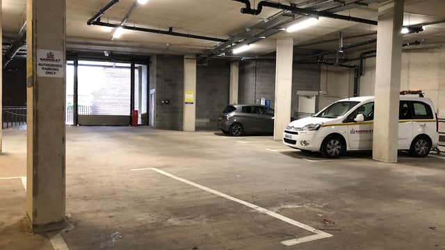 Electric vehicle charging station in a parking garage with two parked cars and visible signage.