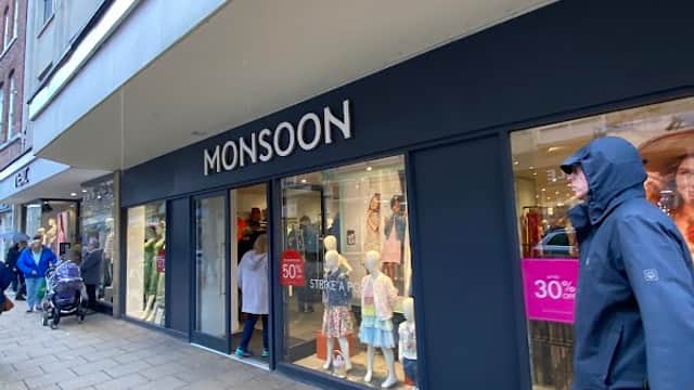 Monsoon shop front with large windows displaying clothing, shoppers walking by on a rainy day in York.