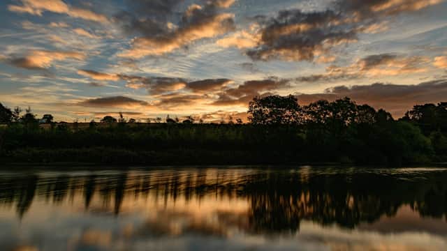 Sunset over Ulley Country Park, reflecting on calm water, with trees silhouetted against a colorful sky.
