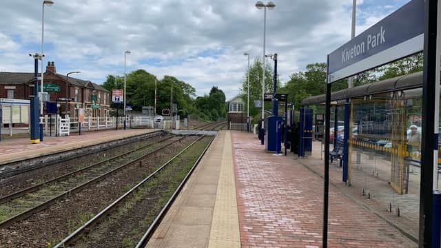 Kiveton Park bus stop with brick pathway, railway tracks, and green trees under a cloudy sky.