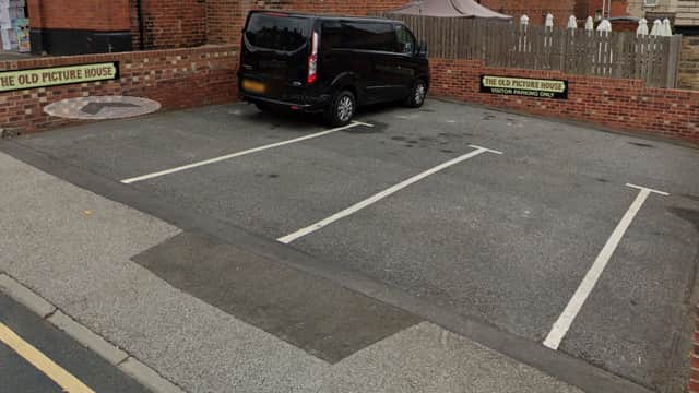 Black van parked in a car park with brick walls, signs for "The Old Picture House," and empty parking spaces.