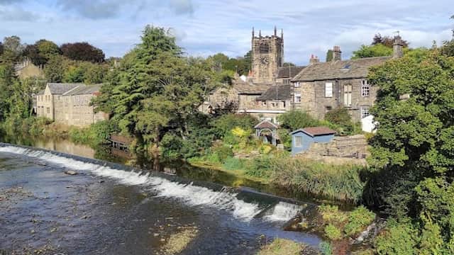 Main Street Car Park in Bingley with a view of a river, trees, and historic buildings under a blue sky.