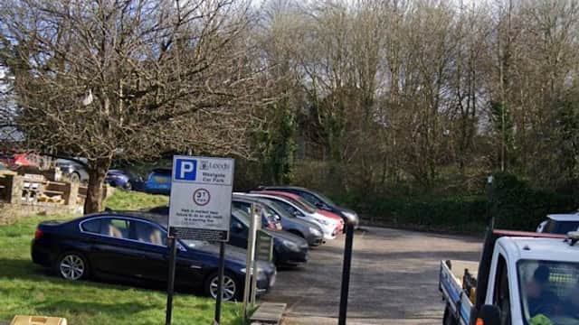 Free parking area with a sign, several parked cars, and a tree under a cloudy sky in Otley, Yorkshire.