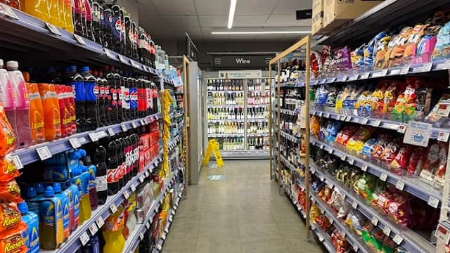 Aisle in a grocery store lined with colorful beverage and snack products, with a caution sign on the floor.