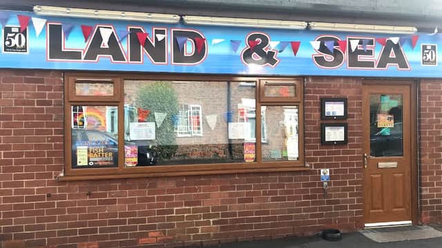 Brightly colored sign reading "LAND & SEA" above a brick restaurant facade with windows and promotional posters.