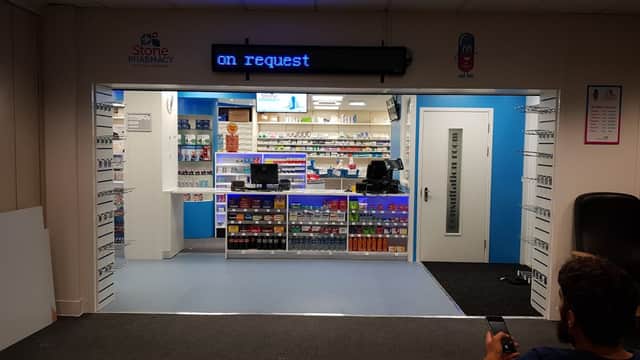 Brightly lit pharmacy entrance with shelves of products, a counter, and a digital sign displaying "on request."