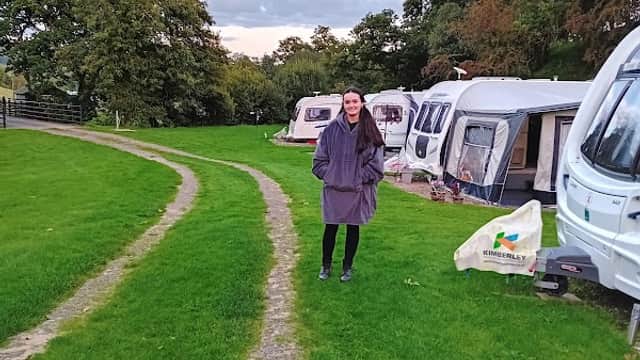 A woman in a purple coat stands on a grassy path beside parked caravans at Low Wood Caravan Park.
