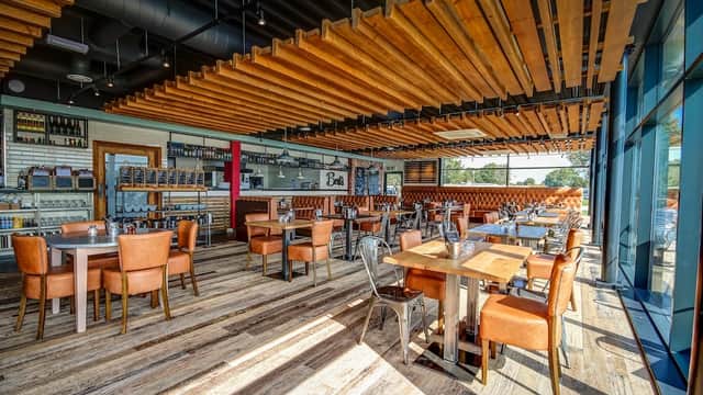 Bright, modern café interior with wooden beams, metal chairs, and tables, featuring a bar and large windows.