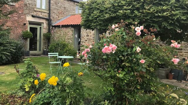 Charming guest house with stone walls, vibrant flower garden, and green seating area under a lush tree.