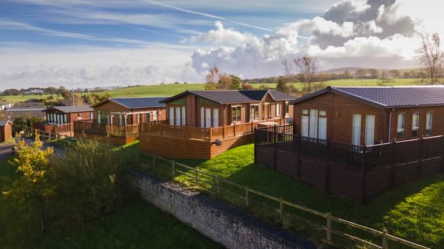 Lodges with wooden exteriors on green hills, surrounded by trees and a blue sky with fluffy clouds at Todber Valley.