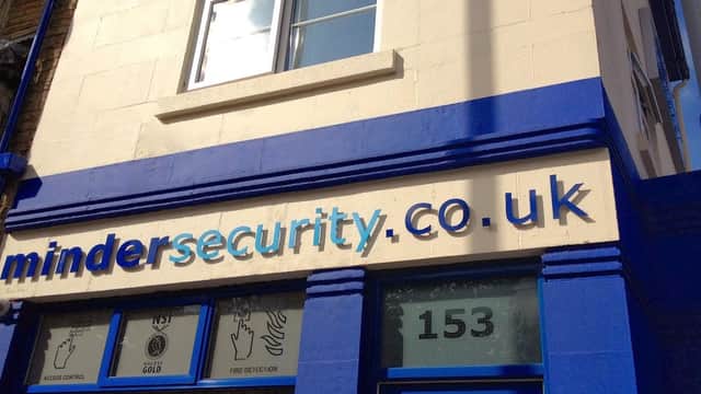 Signage for Minder Security & Fire, featuring blue and white colors, with website and services listed.