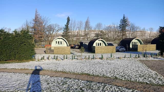 Caravan and campsite with curved cabins, snowy ground, and trees against a clear blue sky in Burtersett, Yorkshire.