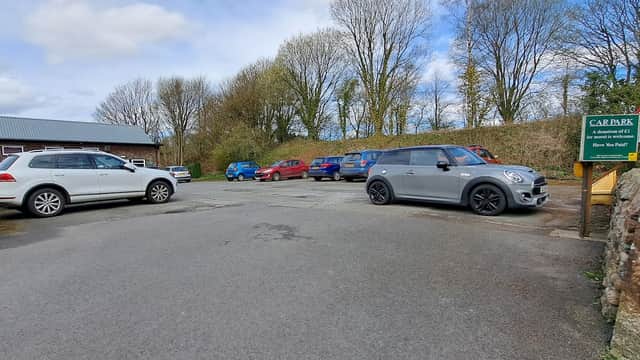 Cowan Bridge Carpark with several parked cars, stone walls, and trees under a partly cloudy sky.