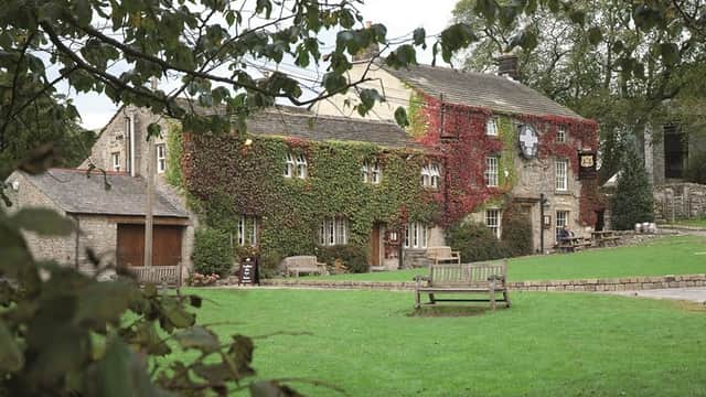 The Lister Arms pub features ivy-covered stone walls, wooden benches, and a lush green lawn in Kirkby Malham, Yorkshire.