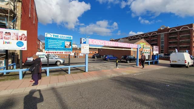 Grange Road Car Park with signage for long and short stays, vehicles parked, and pedestrians walking. Blue sky above.